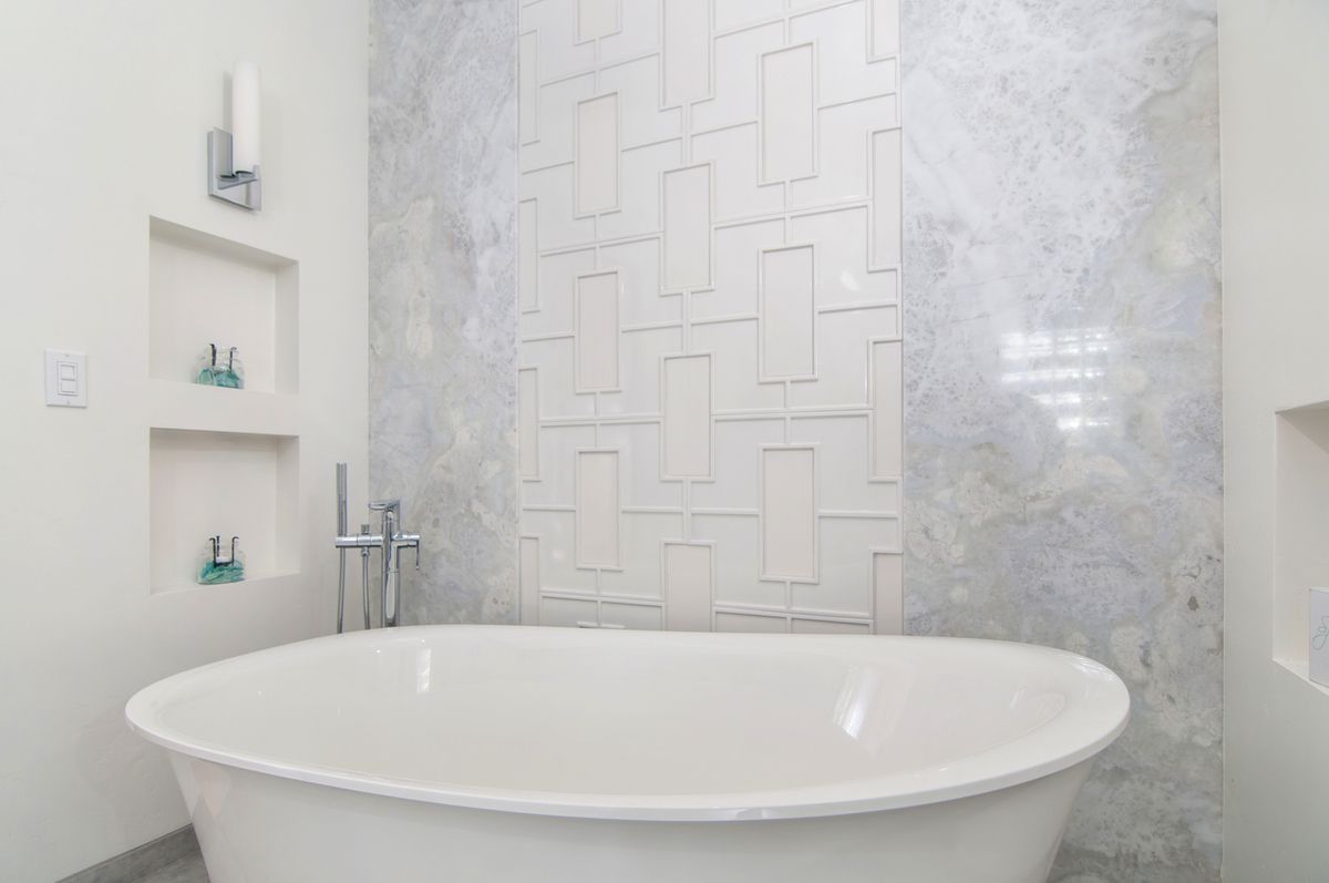 A white bathtub is sitting in a bathroom next to a white tiled wall.