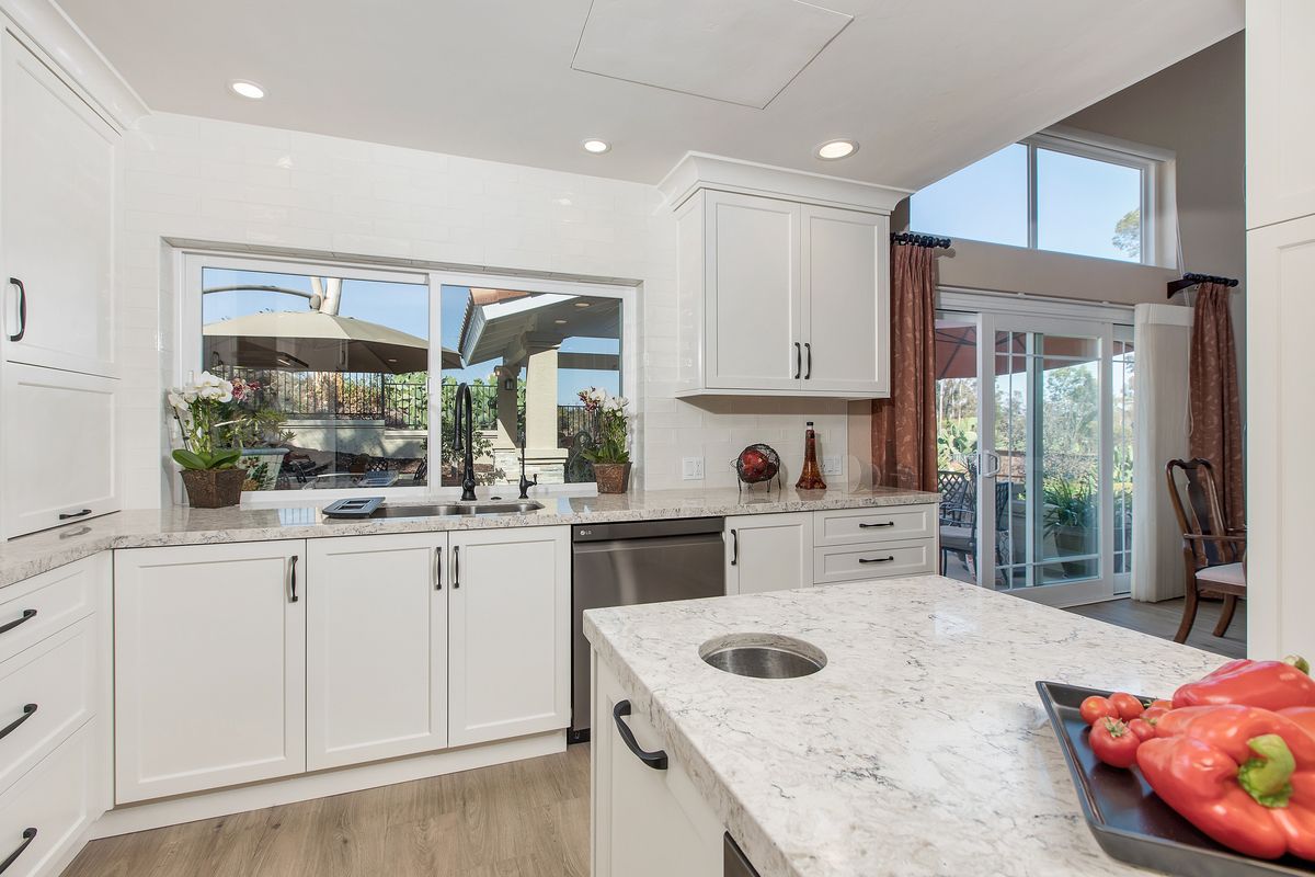 A kitchen with white cabinets and a large island with peppers on it.