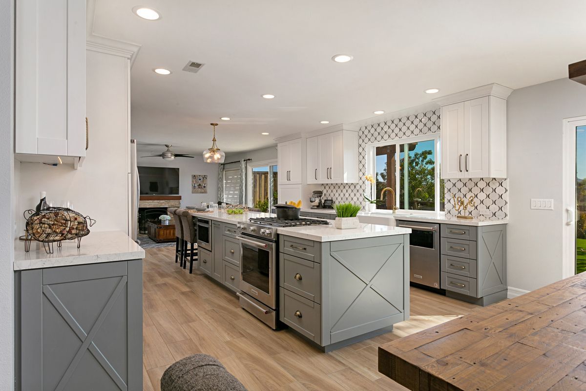 A kitchen with white cabinets , stainless steel appliances , a large island and a wooden table.