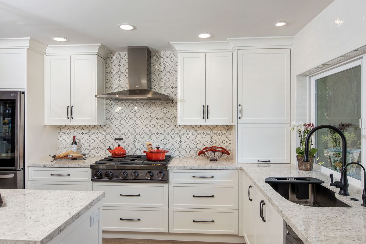 A kitchen with white cabinets , a stove , a sink , and a window.