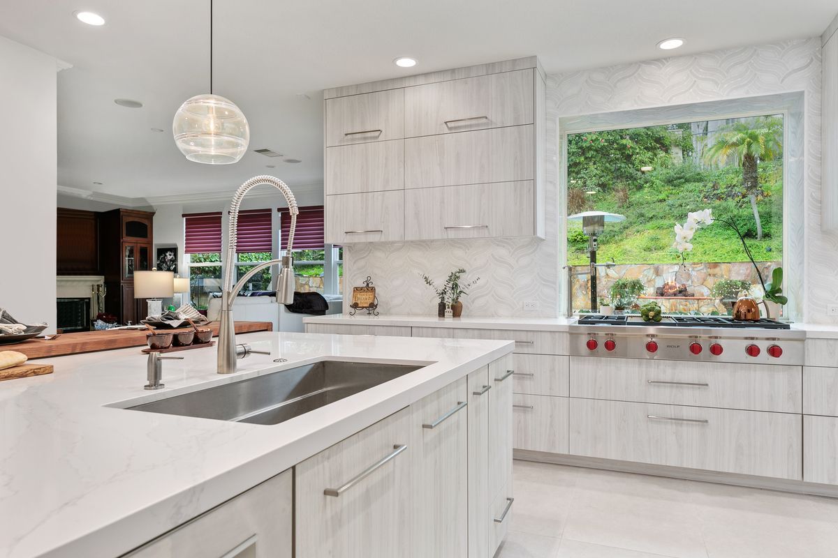A kitchen with white cabinets , stainless steel appliances , a sink , and a large window.