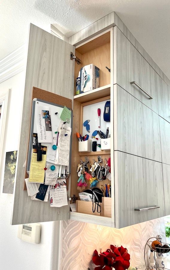 A kitchen cabinet with the door open and a cork board on the wall.