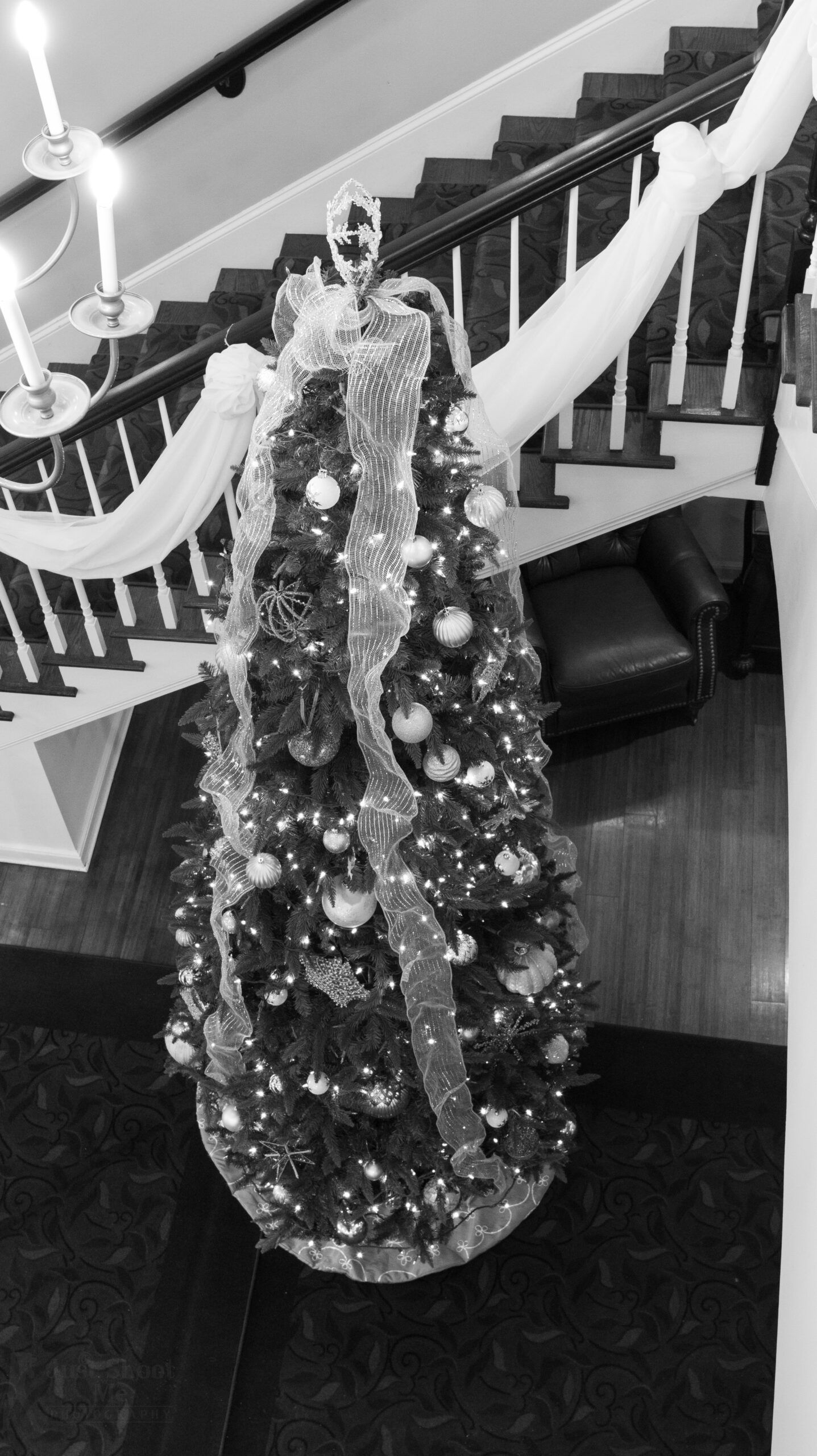 A decorated Christmas tree positioned at the base of a staircase, adorned with ribbons and ornaments.