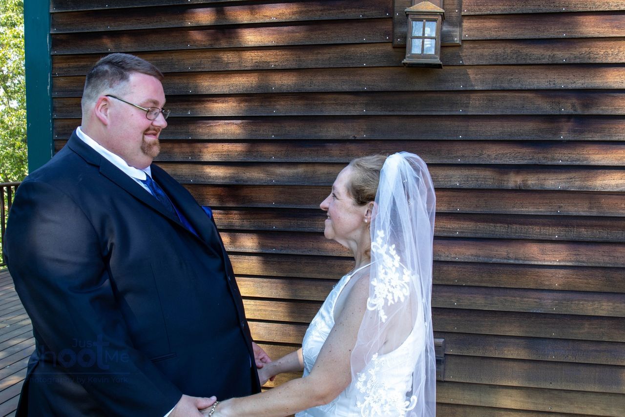 A bride and groom holding hands and smiling at each other in front of a rustic wooden building with a wall lantern.