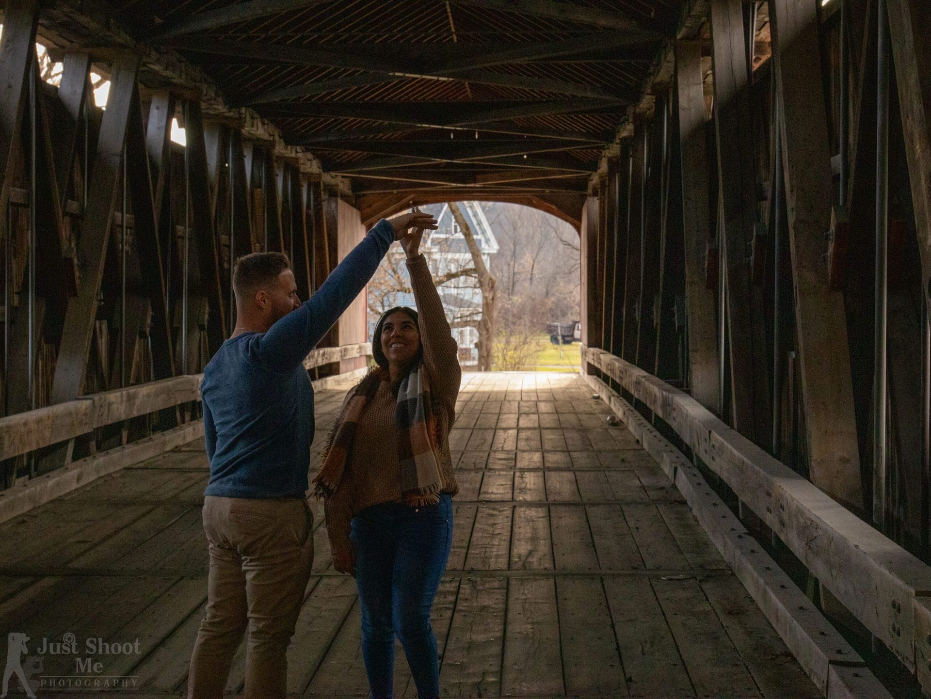 A couple dancing inside a rustic wooden covered bridge, with natural light glowing at the end of the tunnel.