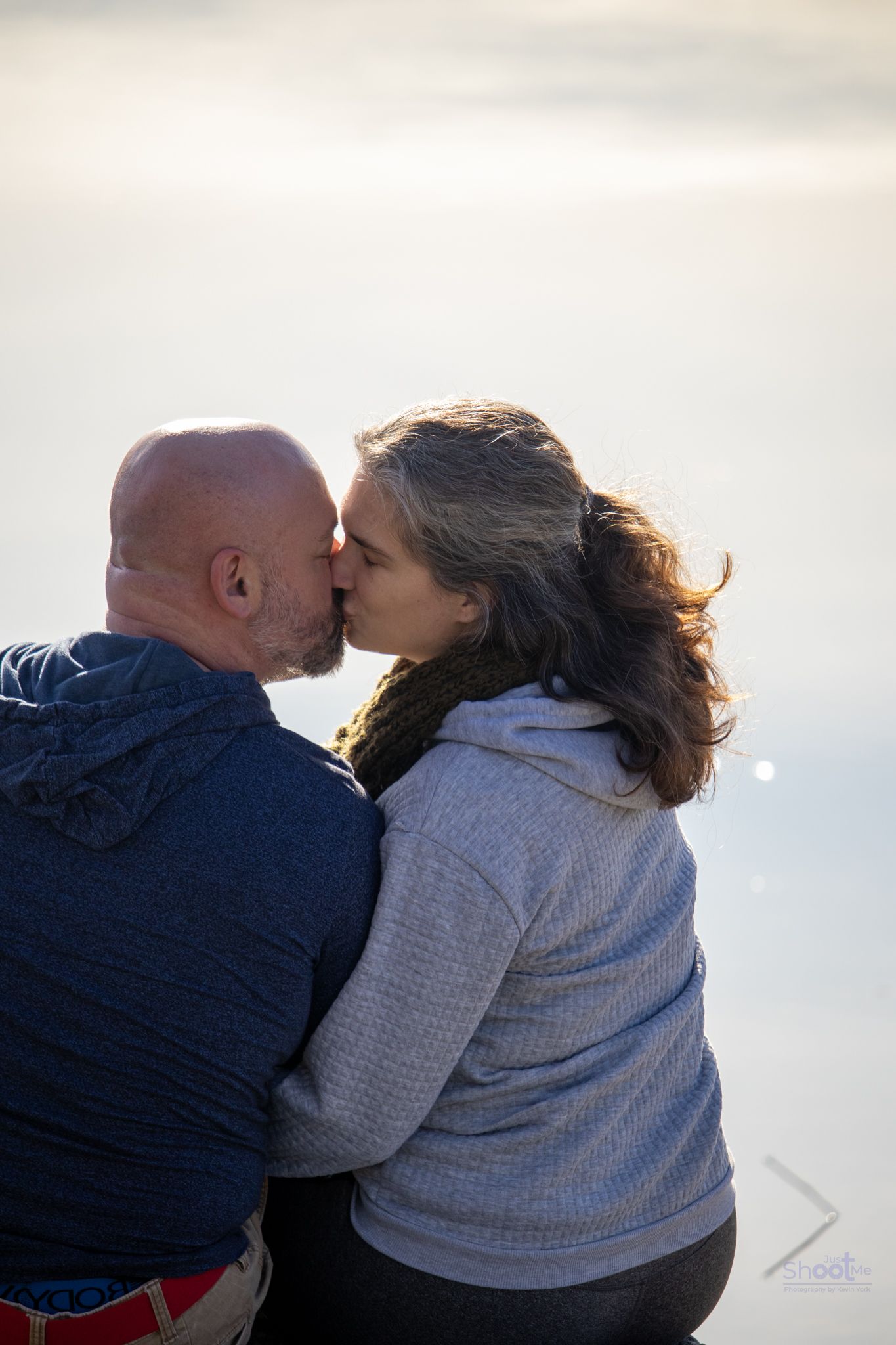 A couple kissing outdoors against a soft, bright, and hazy background.