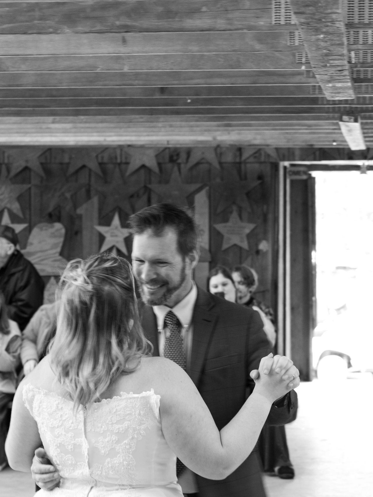 A couple dances together in a rustic wooden building decorated with stars, smiling at each other.