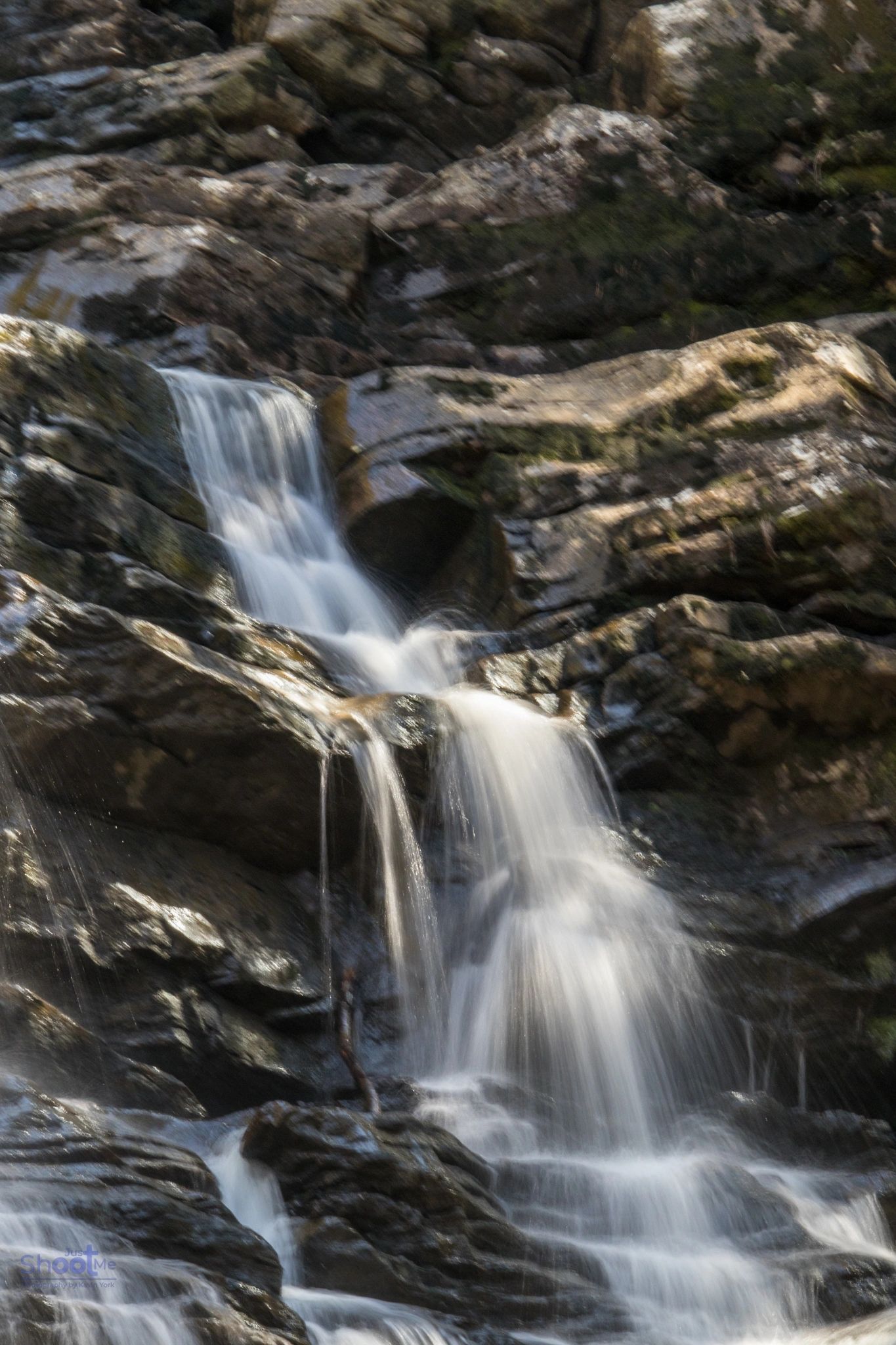 A waterfall cascades over textured dark rocks in a forest setting.