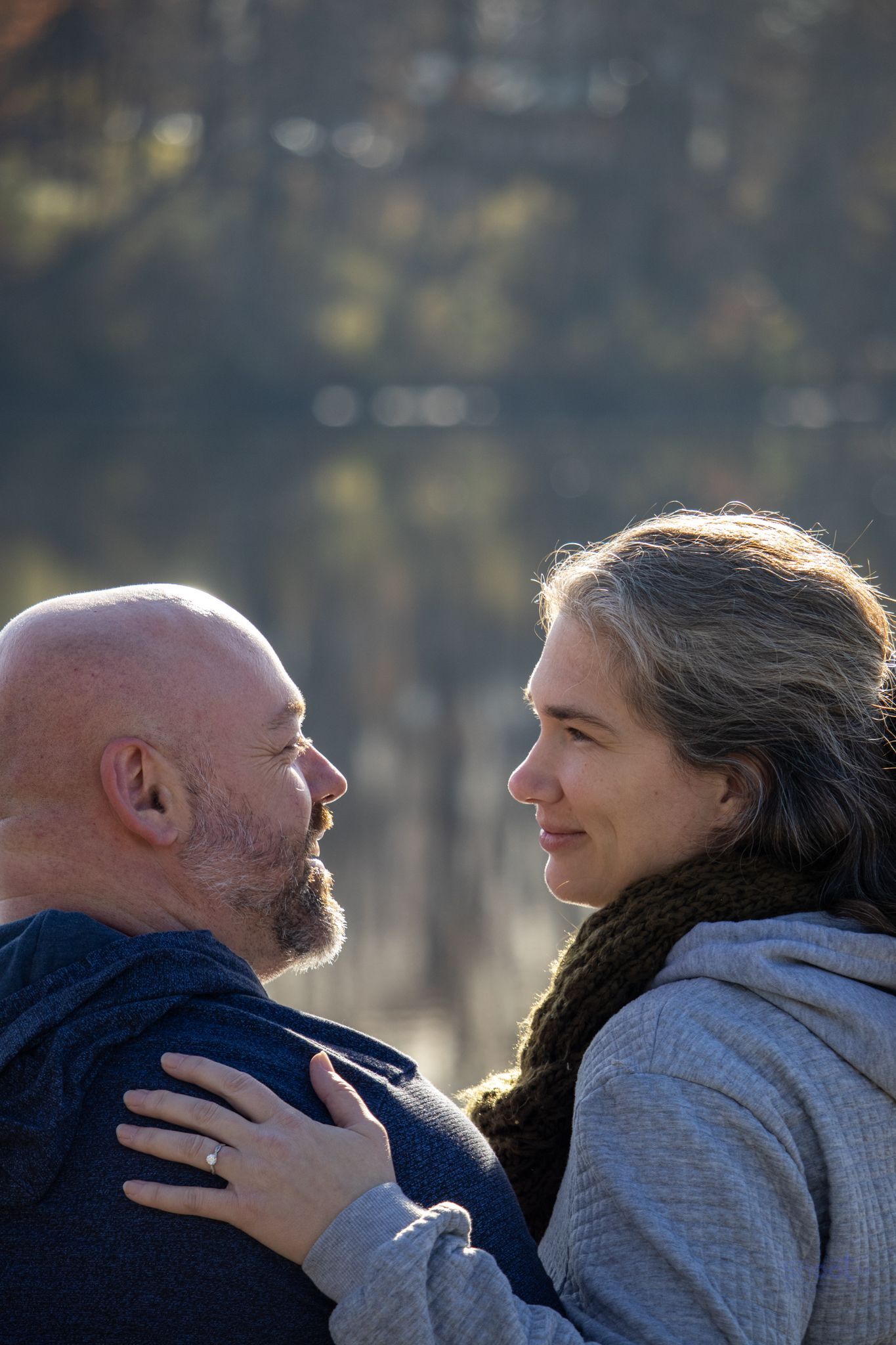 Two people face each other in profile, appearing affectionate with one hand resting gently on the other’s shoulder.
