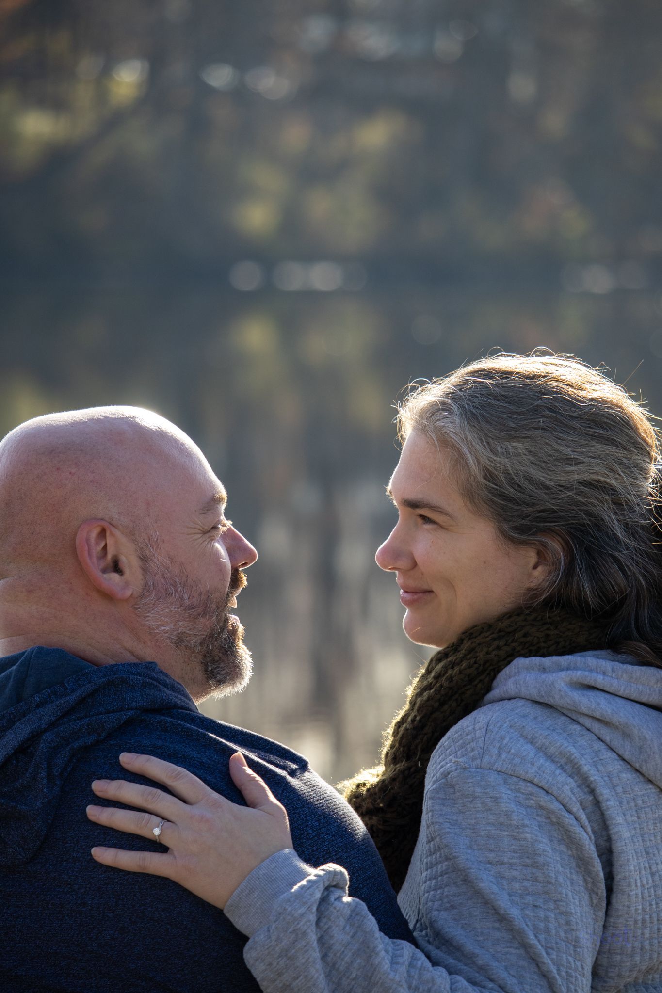 A couple gazes lovingly at each other, standing outdoors in soft, natural light.