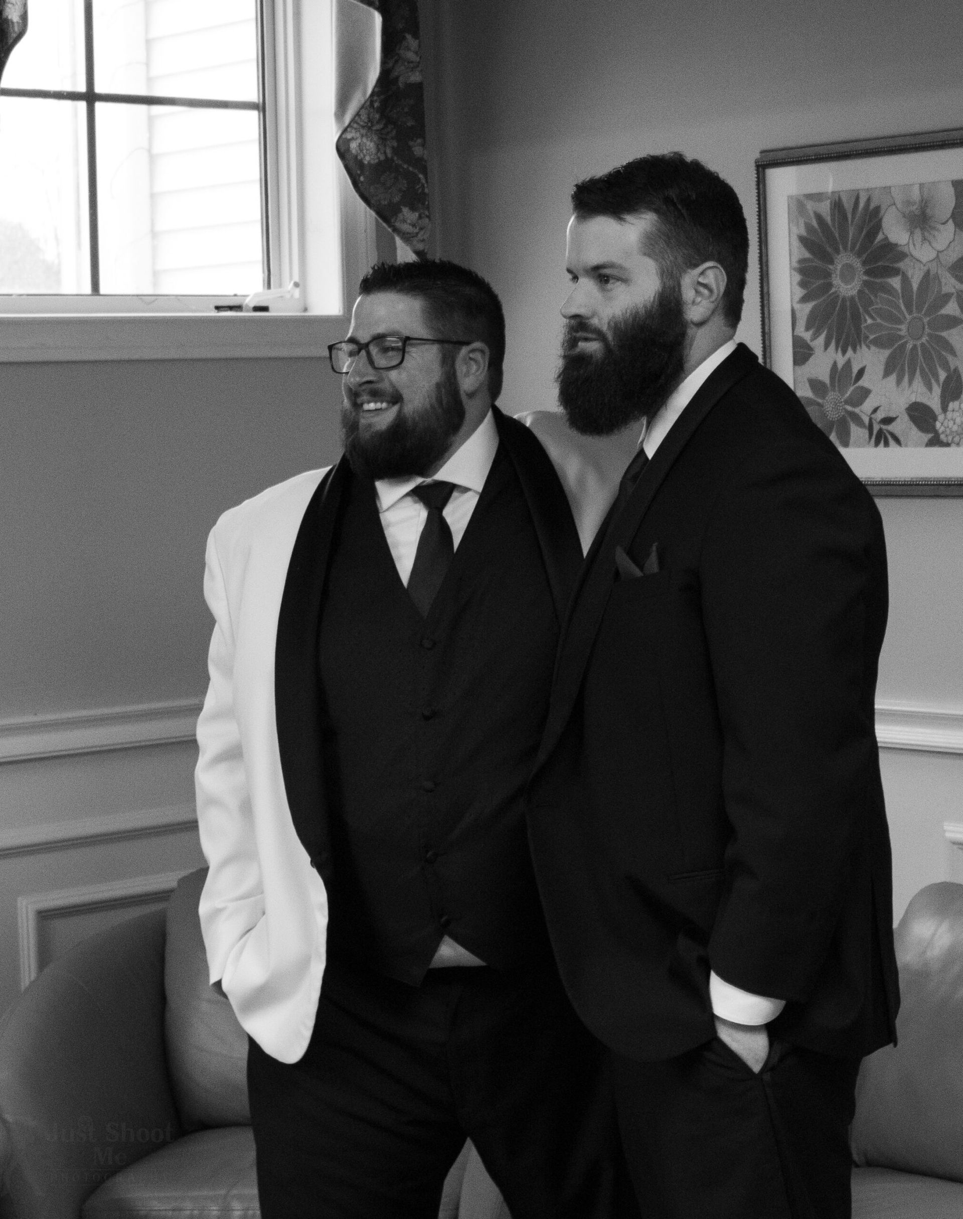 Two men in formal suits, one in a white jacket and one in black, smiling and standing together indoors.