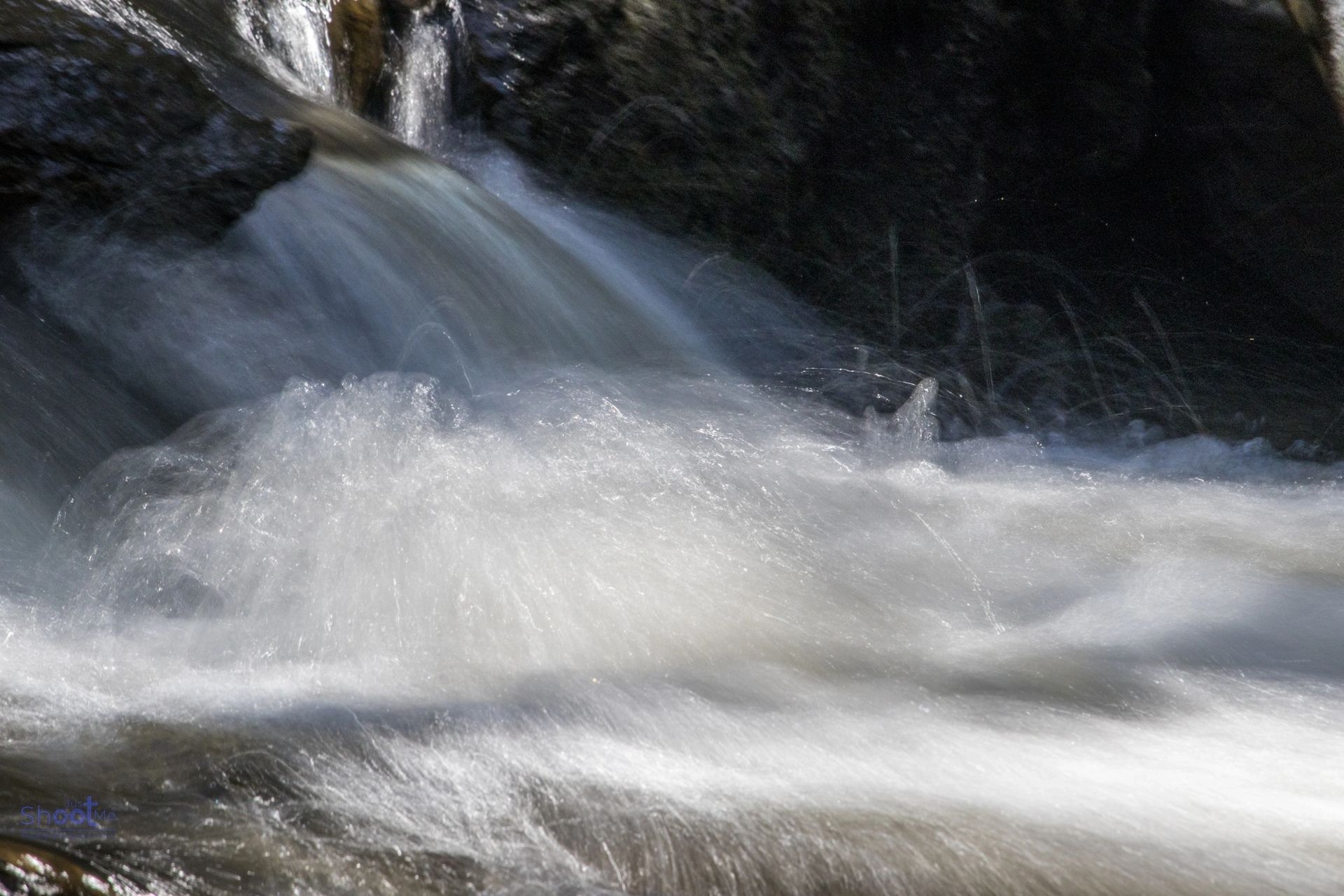 A close-up view of water cascading over dark rocks, creating a blurred, foamy white current.