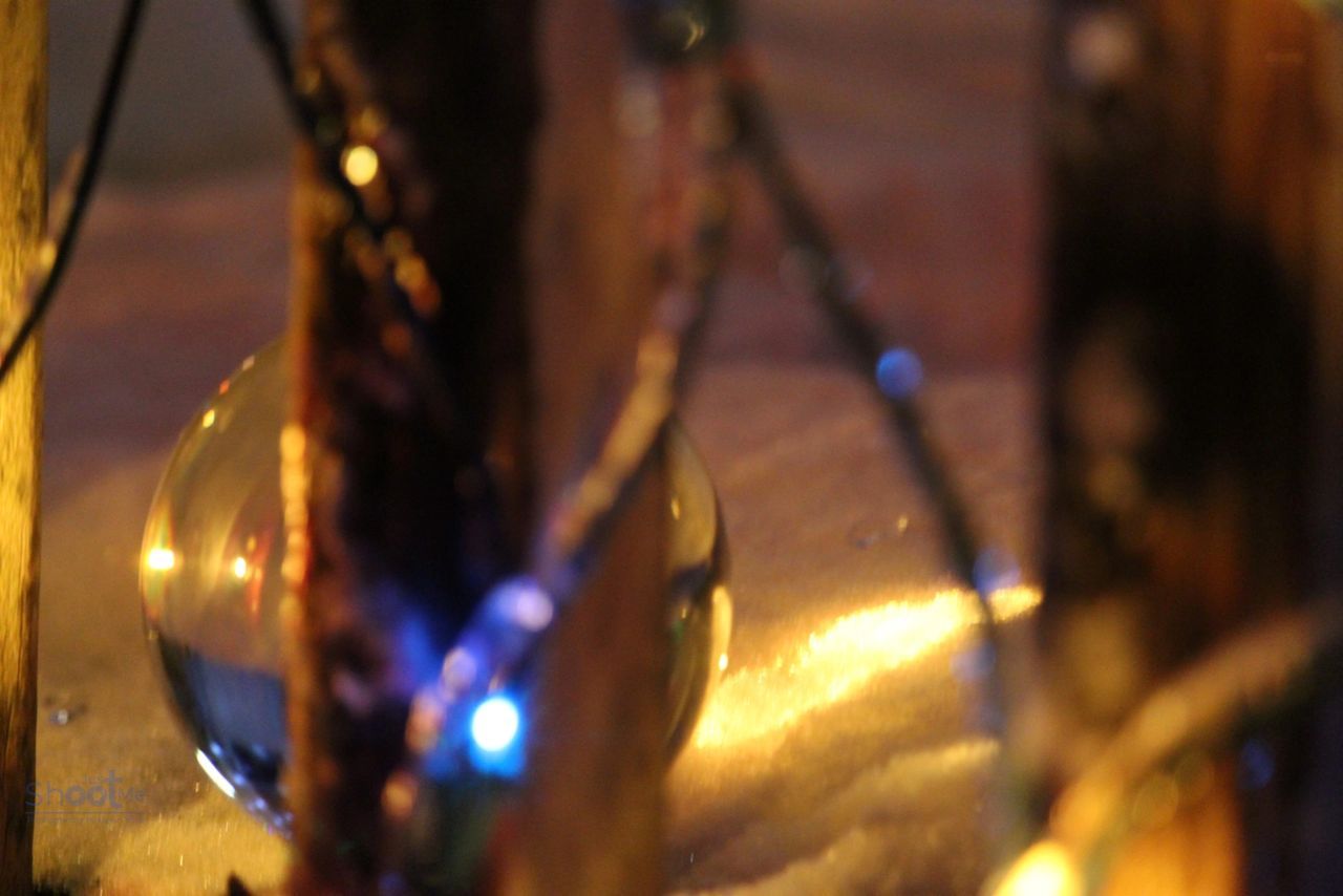 A clear crystal sphere sits behind a wooden board, surrounded by blurry blue and warm yellow fairy lights in the dark.