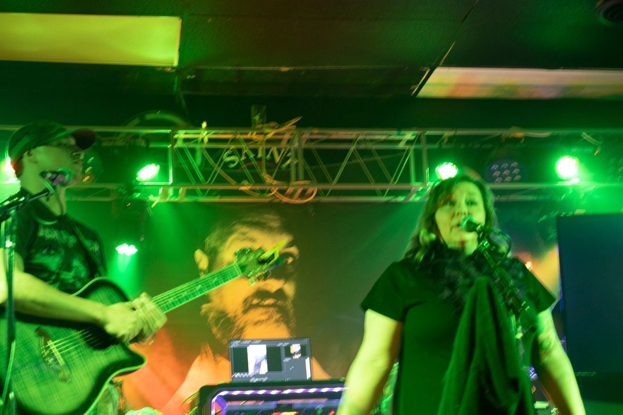 A person playing an electric guitar and a person singing on a stage lit with bright green lights.