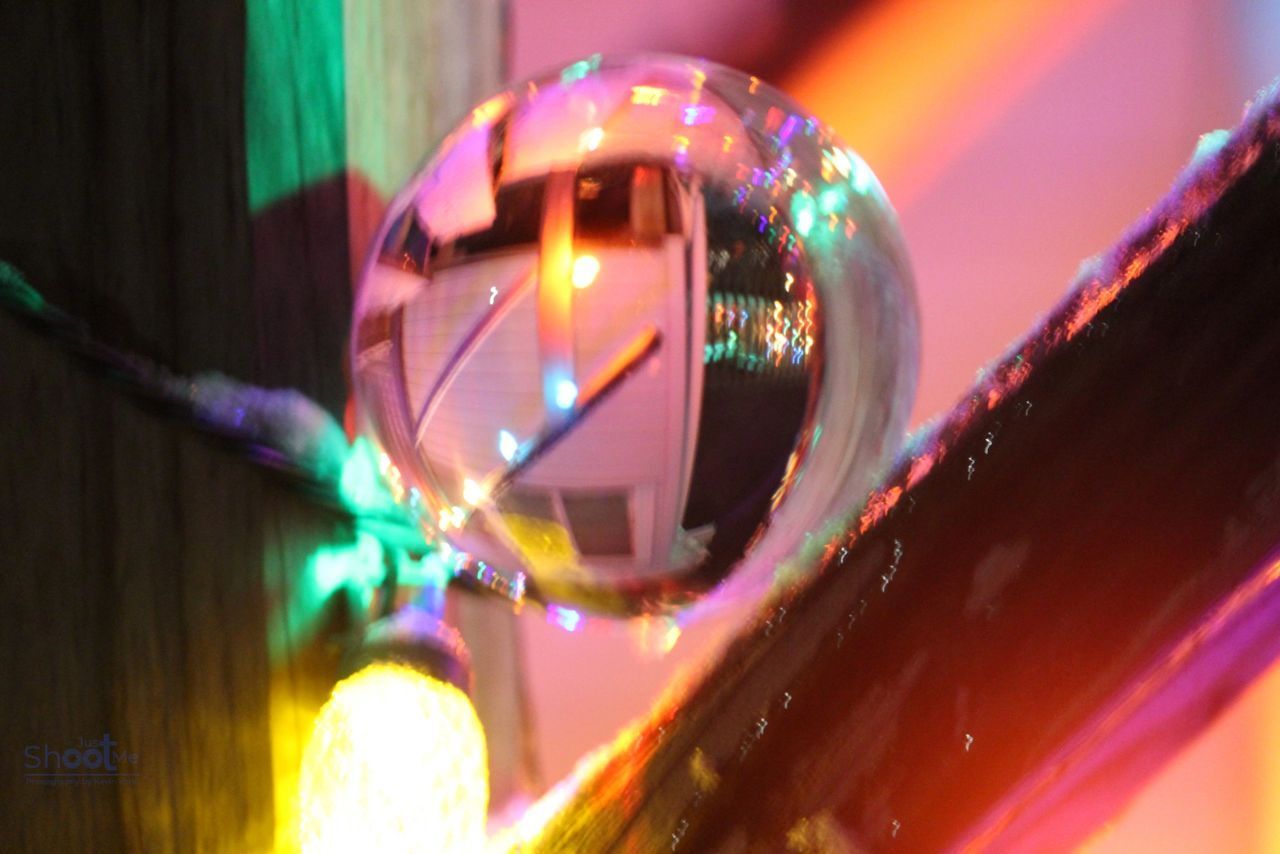 A reflective glass sphere hanging near wooden beams, decorated with colorful, glowing holiday lights.