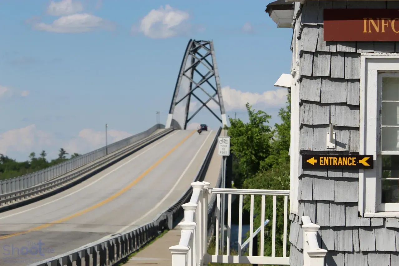 A high-arched bridge spans water, viewed from beside a gray shingled building with an 
