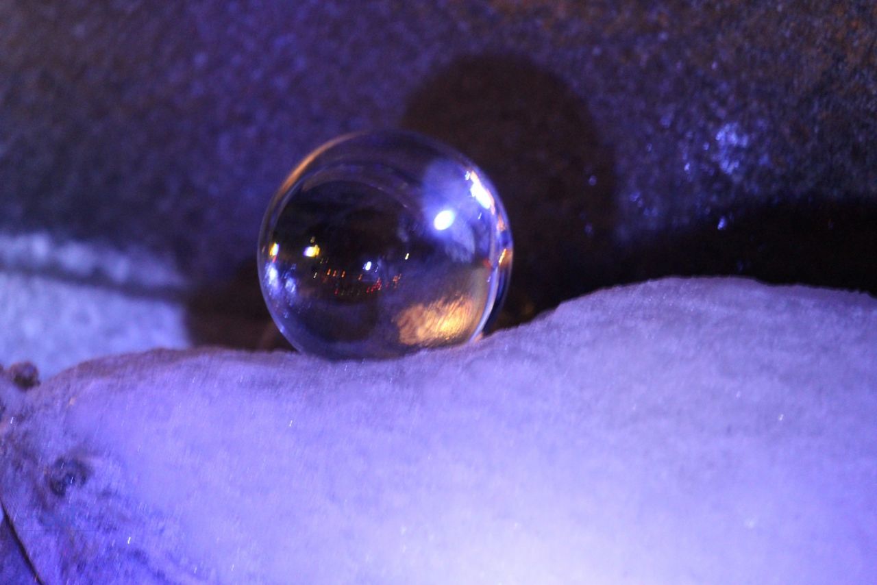 A translucent sphere rests on a textured, light-colored surface under a purple glow, with a dark background.