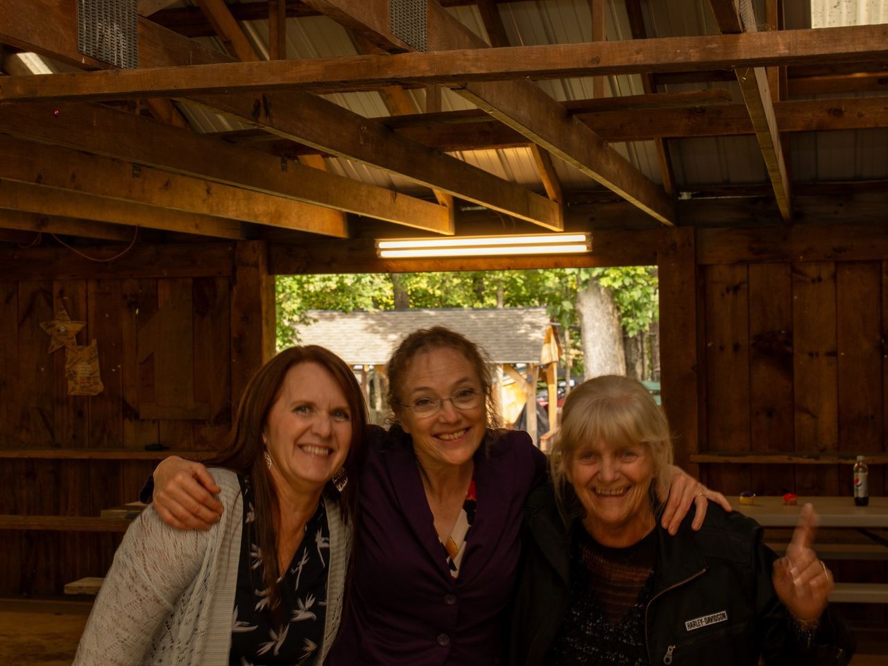Three people smiling and posing for a photo inside a rustic, wooden-framed shelter.