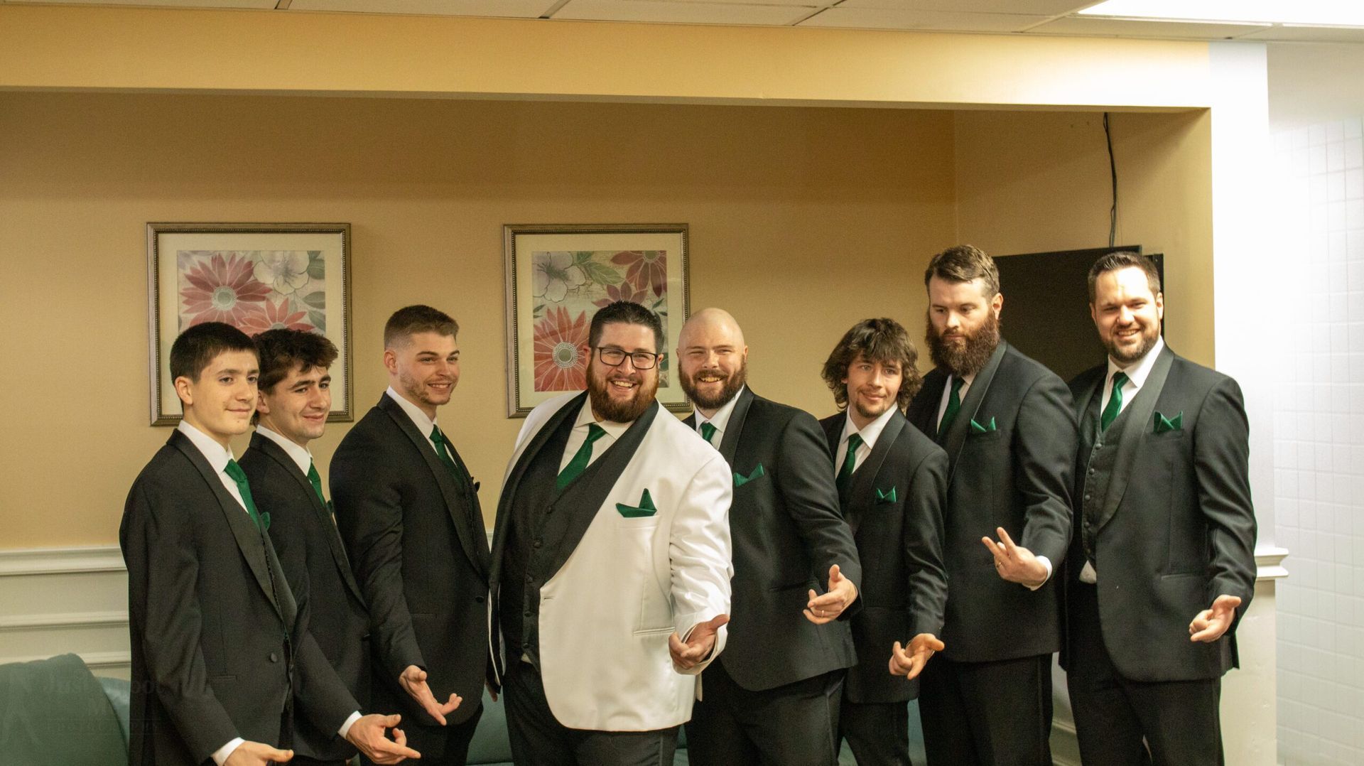 A group of nine men wearing suits with green ties standing together for a photo in front of two framed pictures.