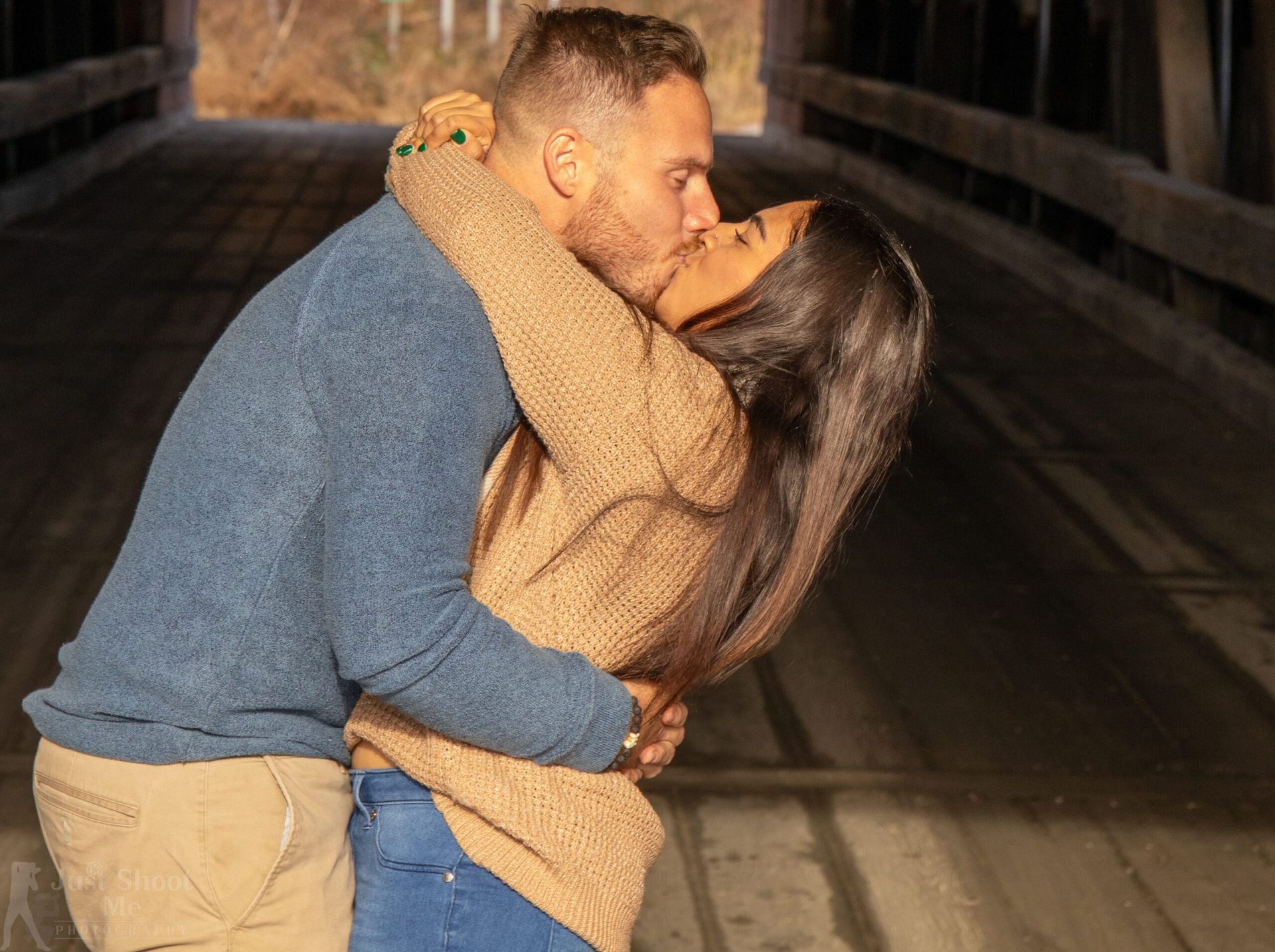 A couple embracing and kissing inside a wooden covered bridge.