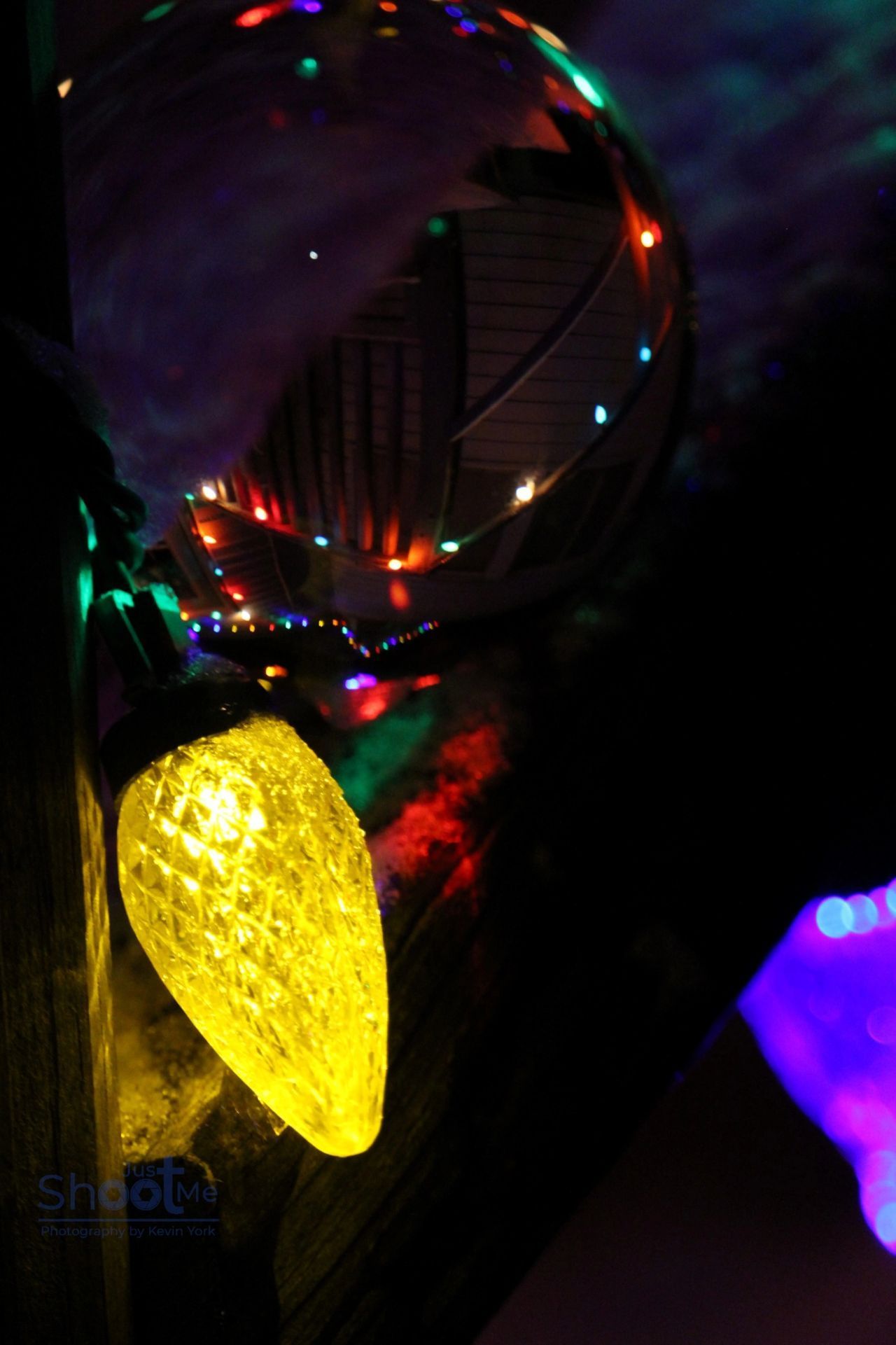 Close-up of a glowing yellow Christmas light bulb against a dark background with blurred, colorful lights.