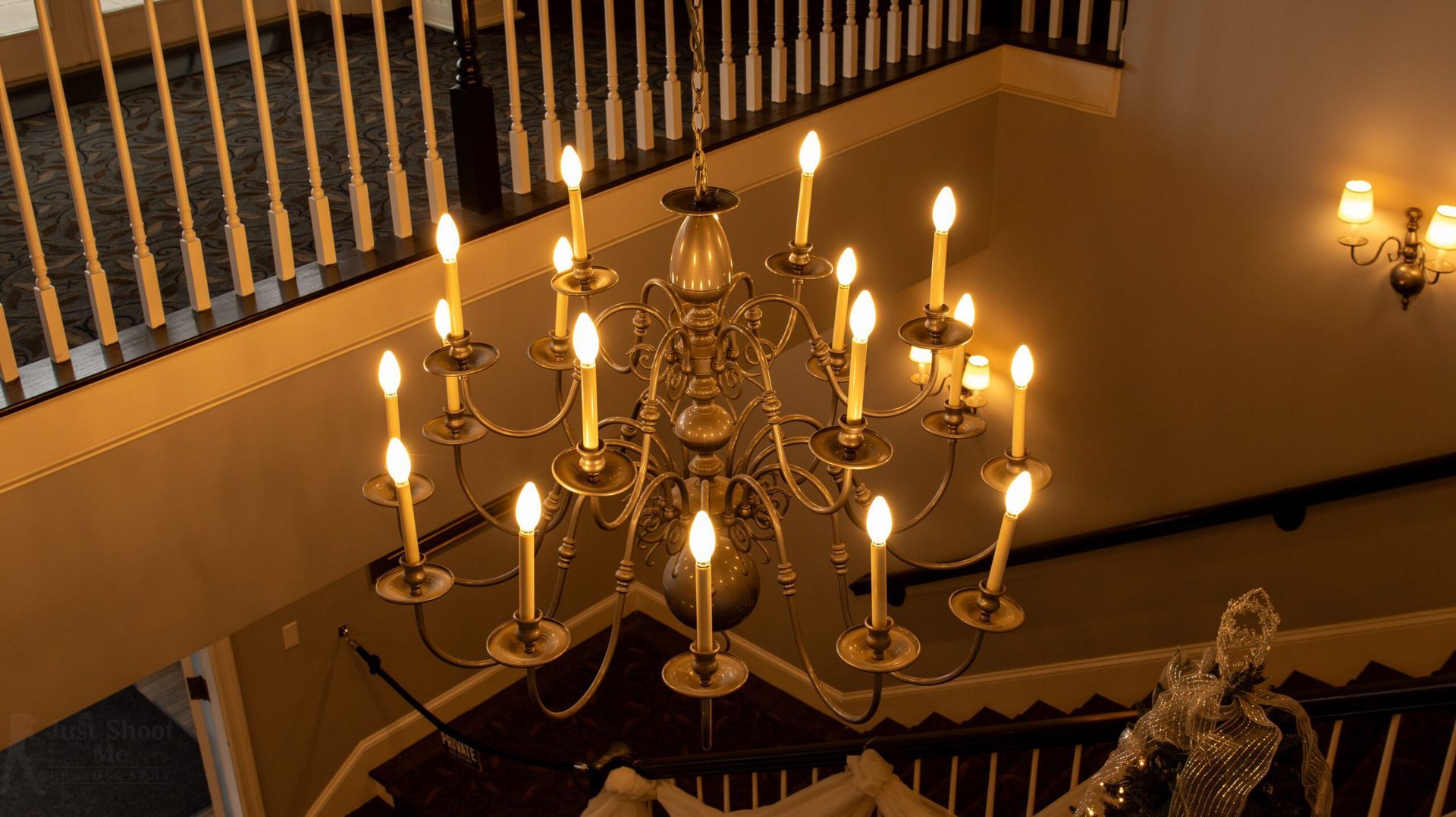 A multi-tiered gold chandelier illuminates an indoor staircase with a white wooden railing.