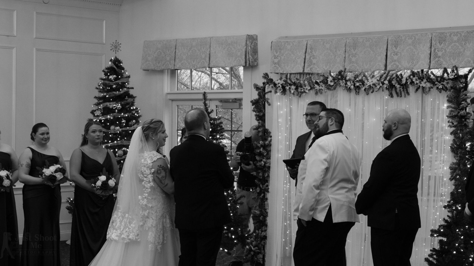 A wedding ceremony with a couple standing before an officiant, flanked by bridesmaids and groomsmen in a decorated room.