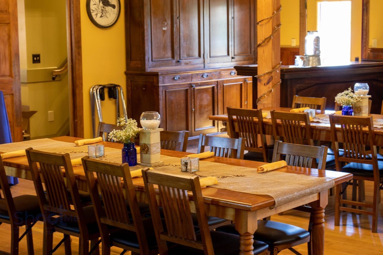 A dining room featuring two long wooden tables with brown chairs set for guests, with a large hutch against the back wall.