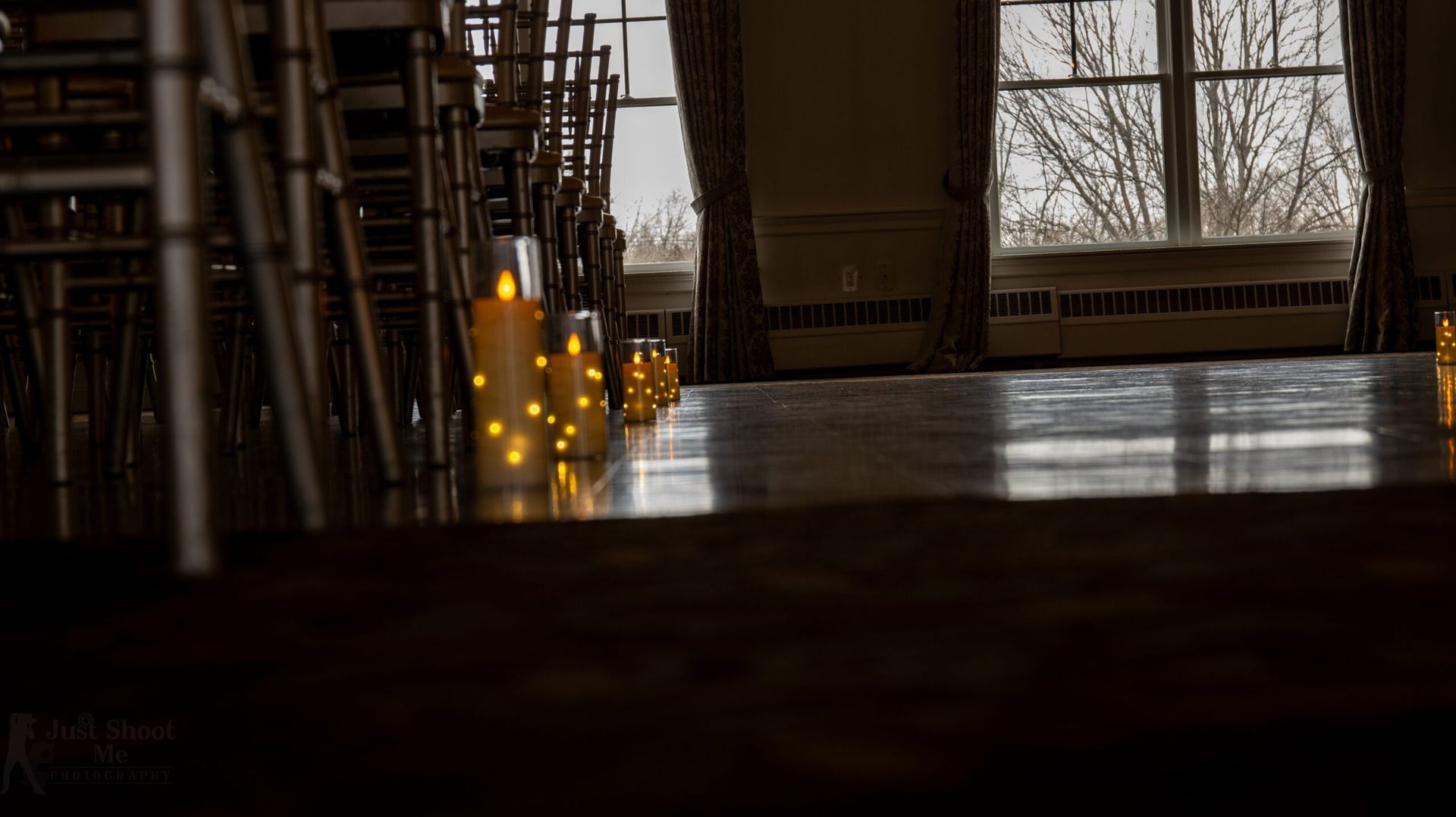 Low-angle view of glowing LED candles along an aisle between rows of chairs in a dimly lit, elegant room.
