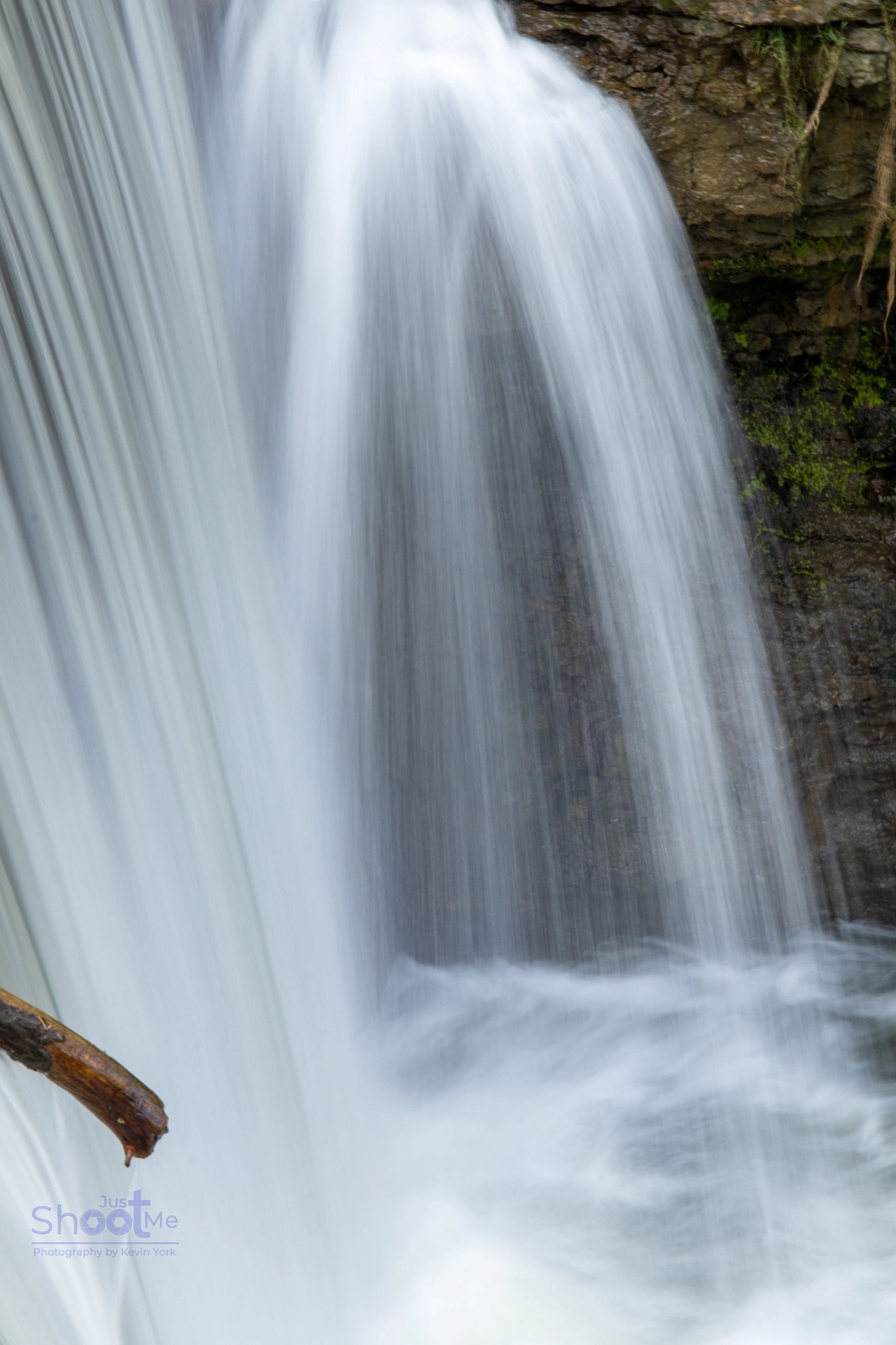 A long-exposure shot of a waterfall cascading over dark, mossy rocks, creating a smooth, white flow of water.