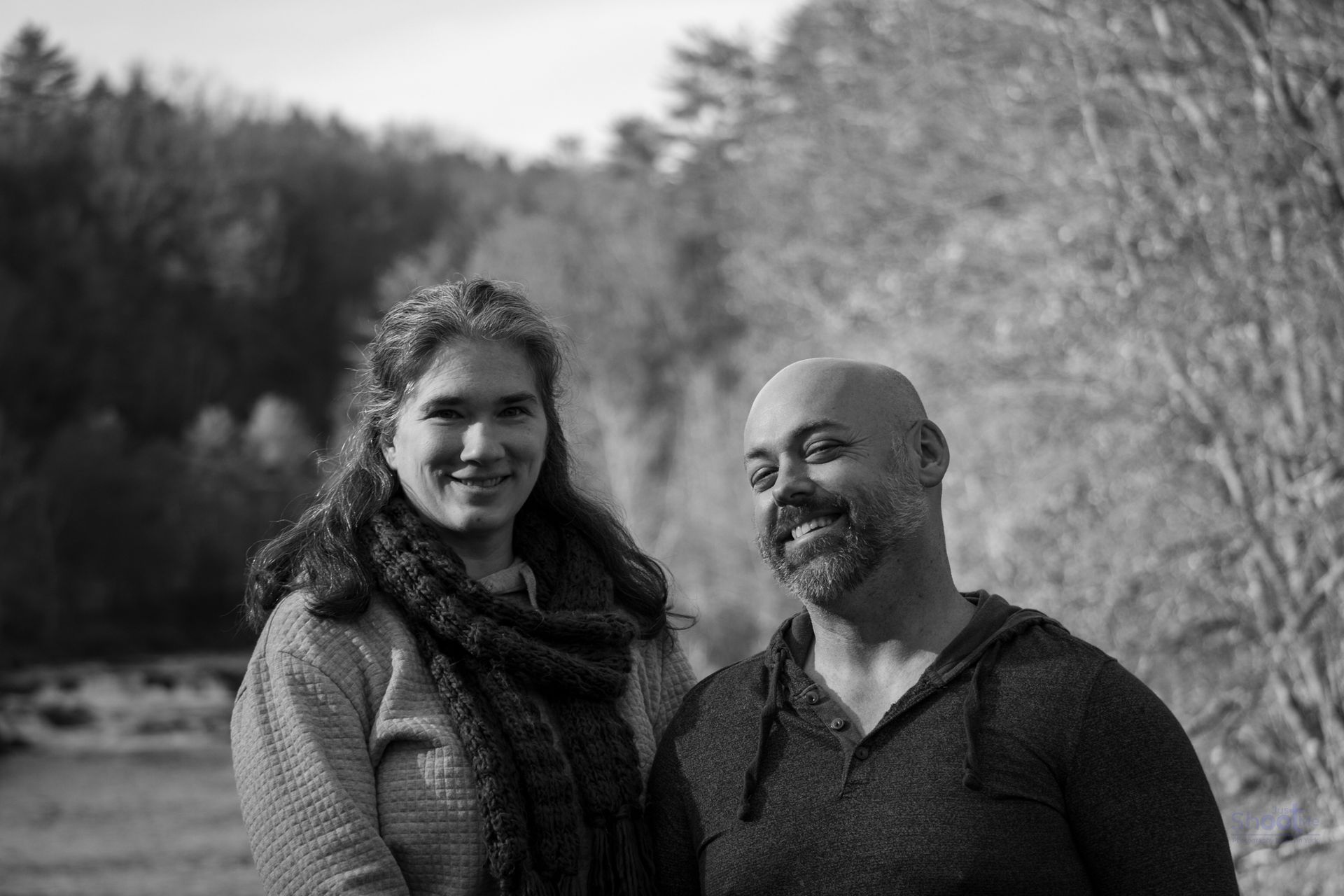 A woman and a man standing side-by-side in a park, smiling at the camera in a black-and-white outdoor portrait.