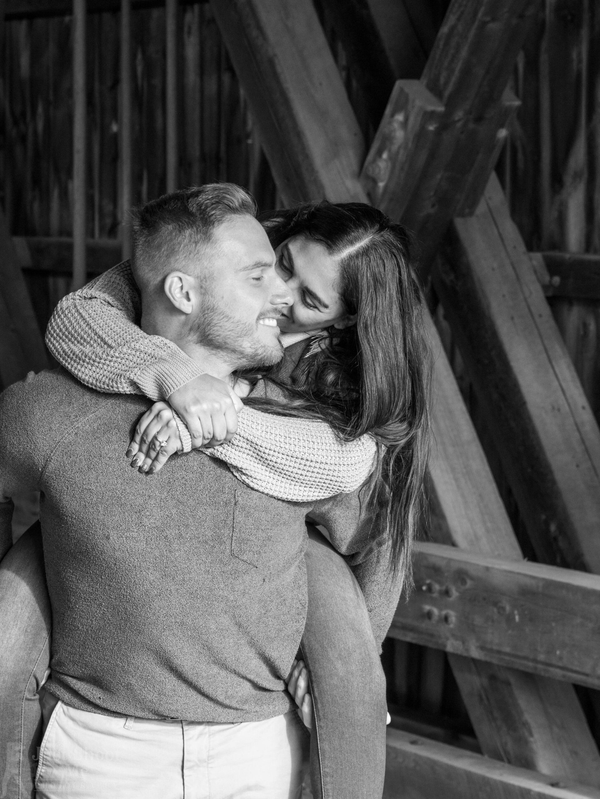 A black-and-white shot of a person giving another person a piggyback ride inside a rustic wooden structure.
