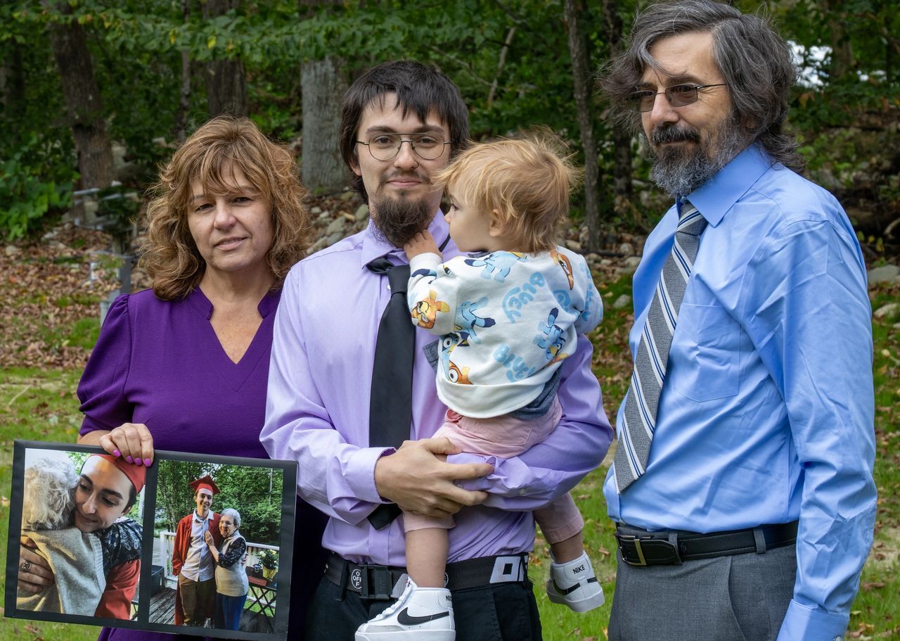 Three adults standing outdoors, one holding a toddler and another holding a photo collage, all facing forward.