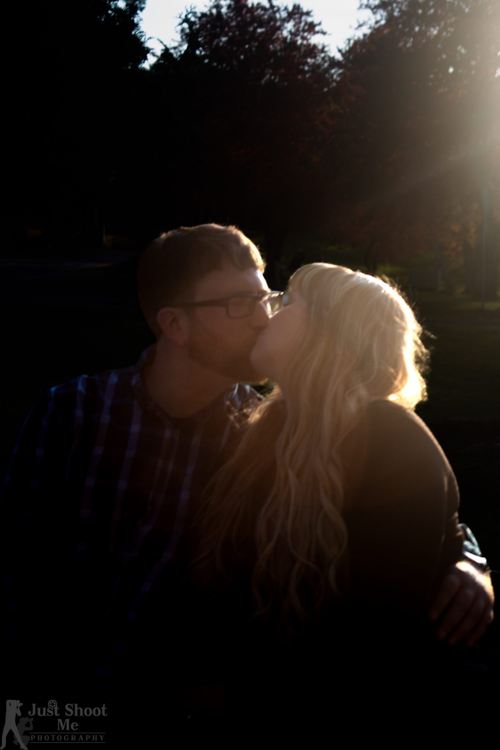 Two people in silhouette kiss against a bright, backlit background.