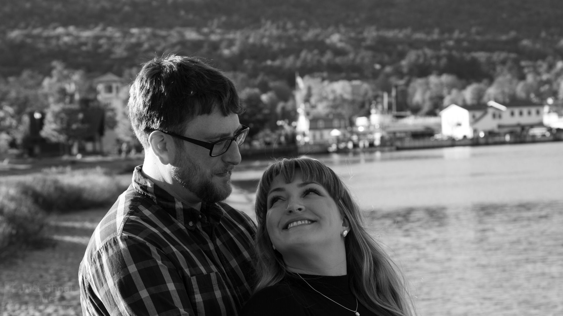 A couple looks affectionately at each other by a body of water in this black-and-white photo.
