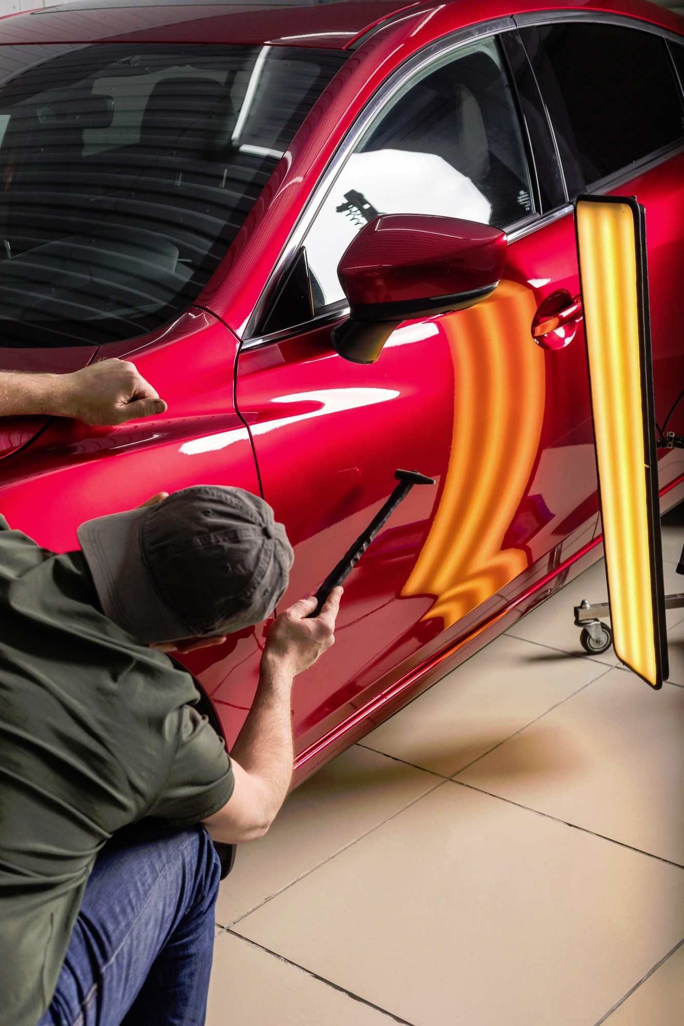 a man is working on a red car with a hammer to remove dents caused by a shopping trolley mishap.