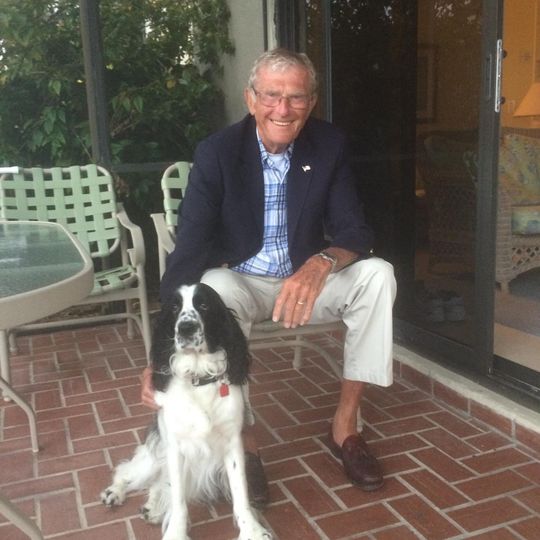Man in blue blazer and dog on a brick patio, smiling.