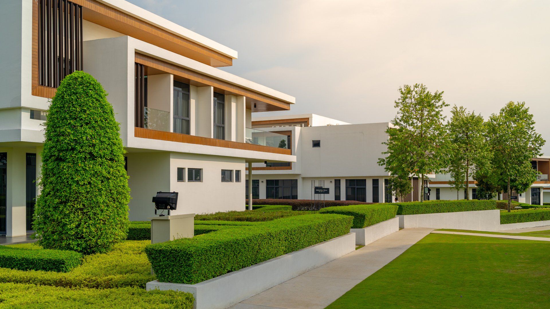 Modern white building with manicured green hedges and lawn.