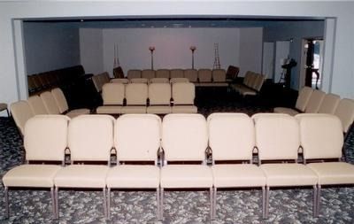 Rows of tan cushioned chairs arranged in a U-shape facing a front wall in a room with patterned carpet.
