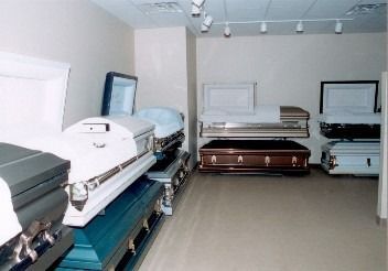 A funeral home showroom featuring multiple open and closed caskets in various colors and finishes arranged on display.
