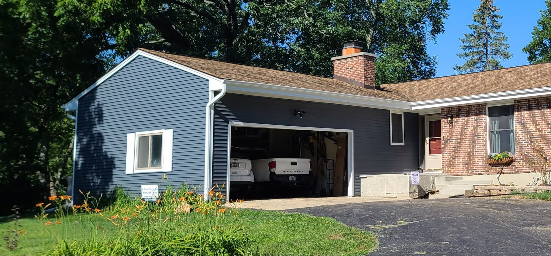 Blue-sided house with attached garage and brown roof; green yard and driveway in front.
