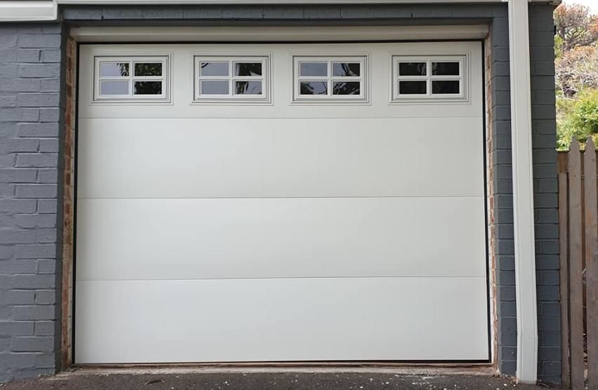 A White Garage Door with Three Windows on A Brick Wall — Illawarra Garage Doors in Dapto, NSW