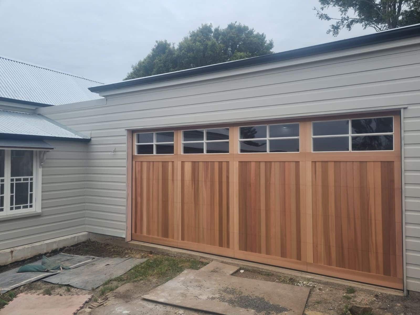 A Wooden Garage Door Is Being Installed on The Side of A House — Illawarra Garage Doors in Albion Park Rail, NSW