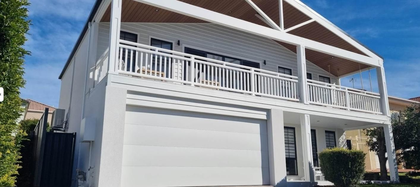 A Large White House with A Balcony and A Garage — Illawarra Garage Doors in Nowra, NSW