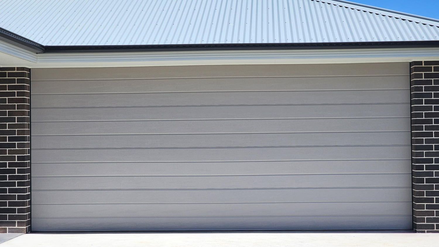 A White Garage Door Is Sitting in Front of A Brick Building — Illawarra Garage Doors in Albion Park Rail, NSW