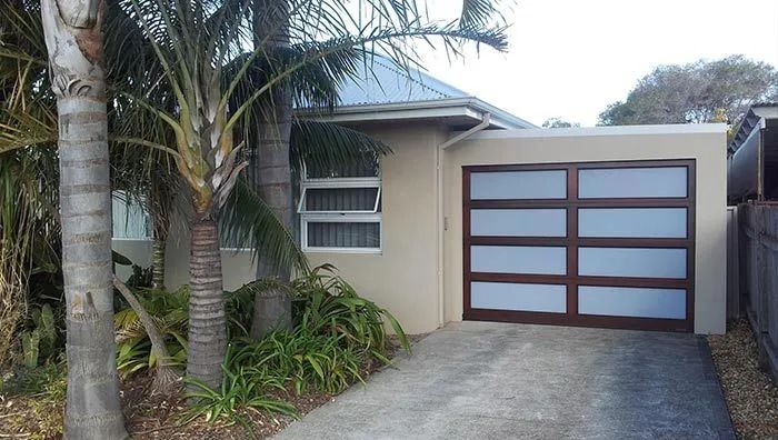 A House with A Garage and Palm Trees in Front of It — Illawarra Garage Doors in Albion Park Rail, NSW