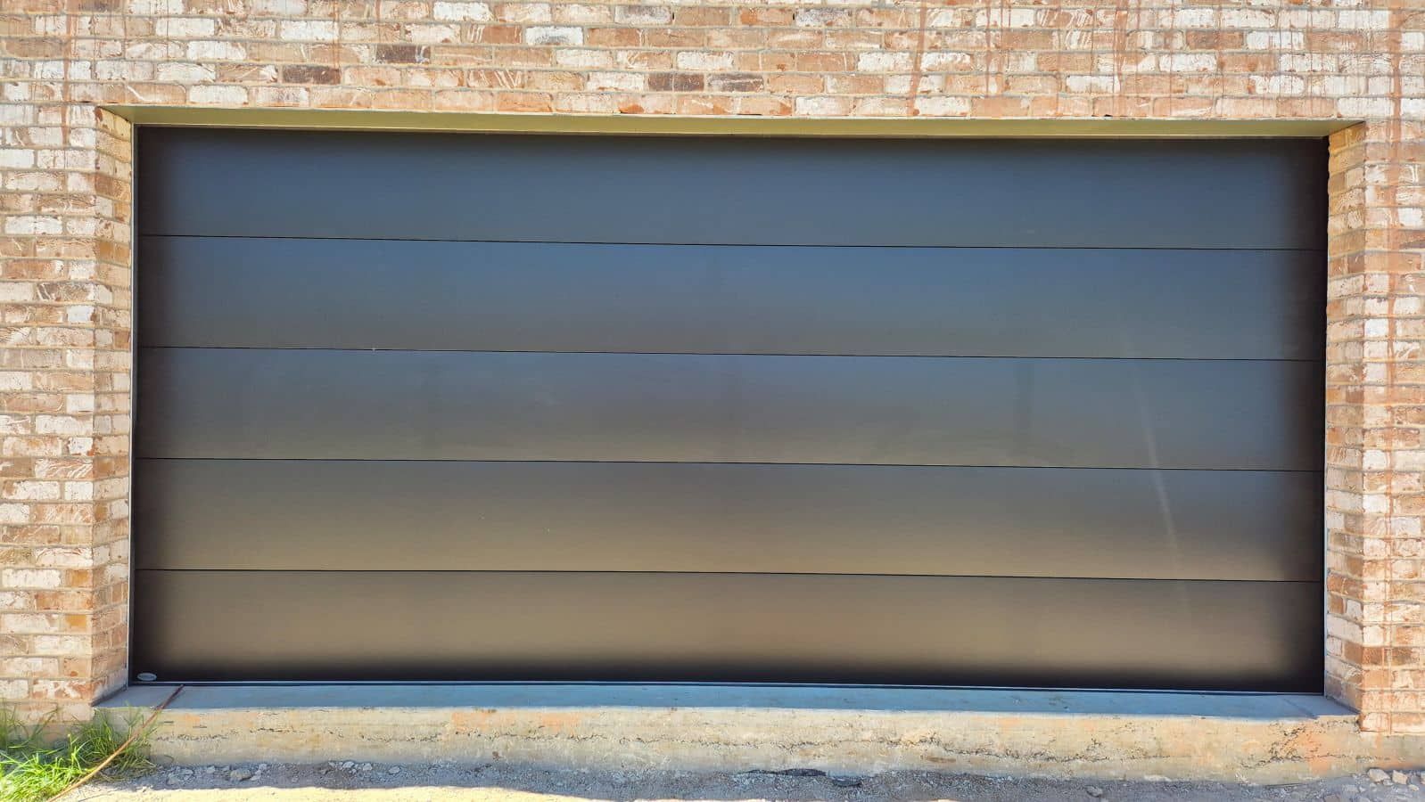 A Black Garage Door Is Sitting in Front of A Brick Building — Illawarra Garage Doors in Albion Park Rail, NSW