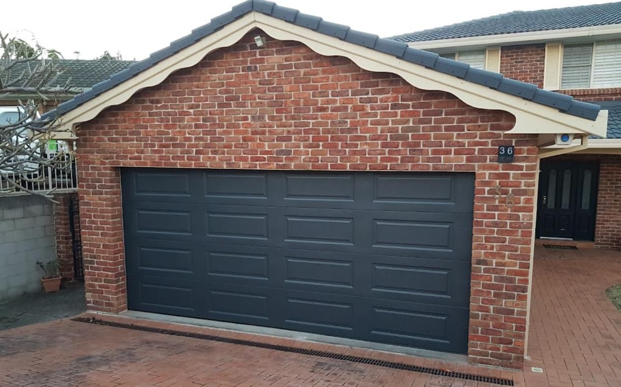 A Brick Garage with A Black Garage Door in Front of A Brick House — Illawarra Garage Doors in Bowral, NSW