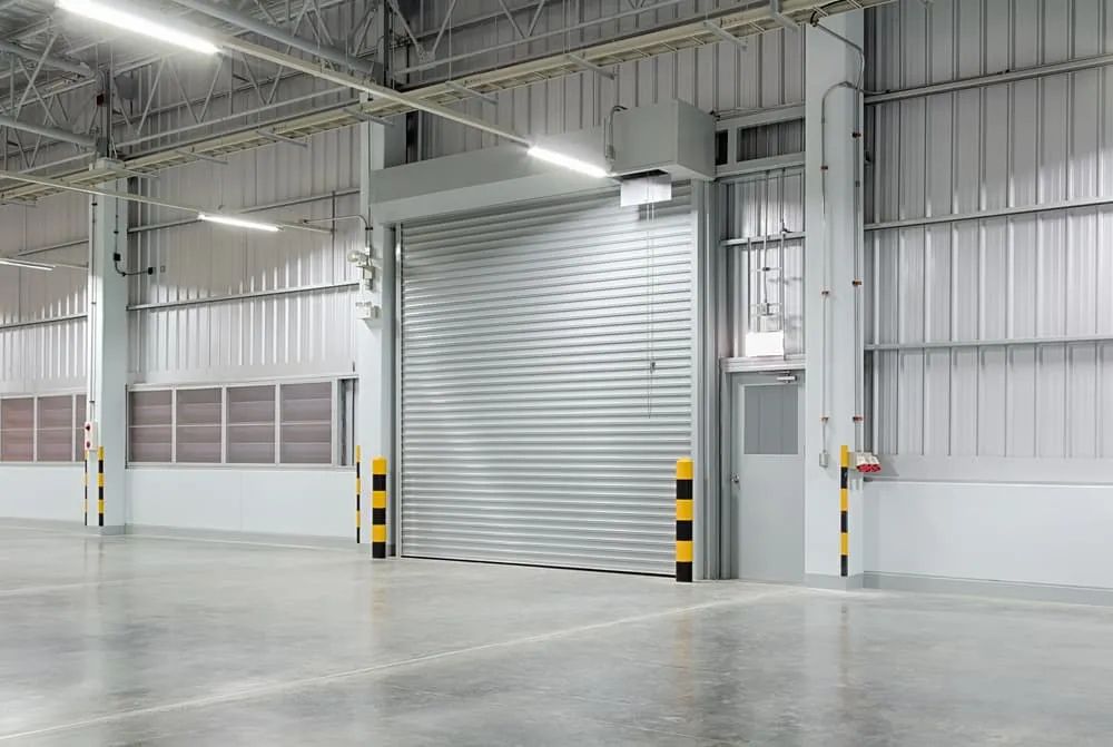 An Empty Warehouse with A Rolling Door and A Concrete Floor — Illawarra Garage Doors in Albion Park Rail, NSW