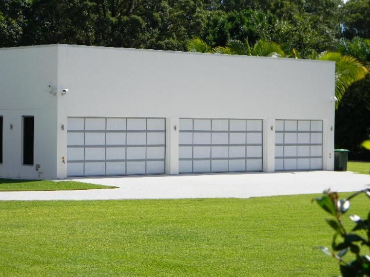 A White Garage with Three White Garage Doors and A Driveway — Illawarra Garage Doors in Albion Park Rail, NSW